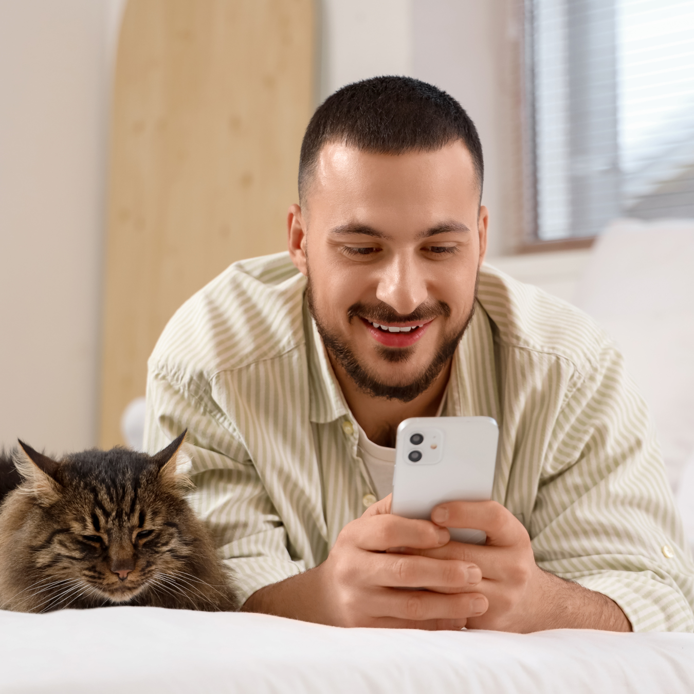 Man lying on a bed with a cat, using a smartphone
